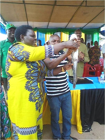 Kishapu District Commissioner (Nyabaganga Talaba) and REDESO staff holding the Catfish kept from UWASALU (Umoja wa Wafuga Samaki Lubaga) fish farming enterprise